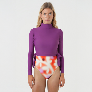 Woman wearing a purple long-sleeve top with a colorful swimsuit underneath