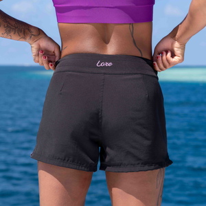 Person wearing black shorts with 'Lore' embroidery against a blue ocean background
