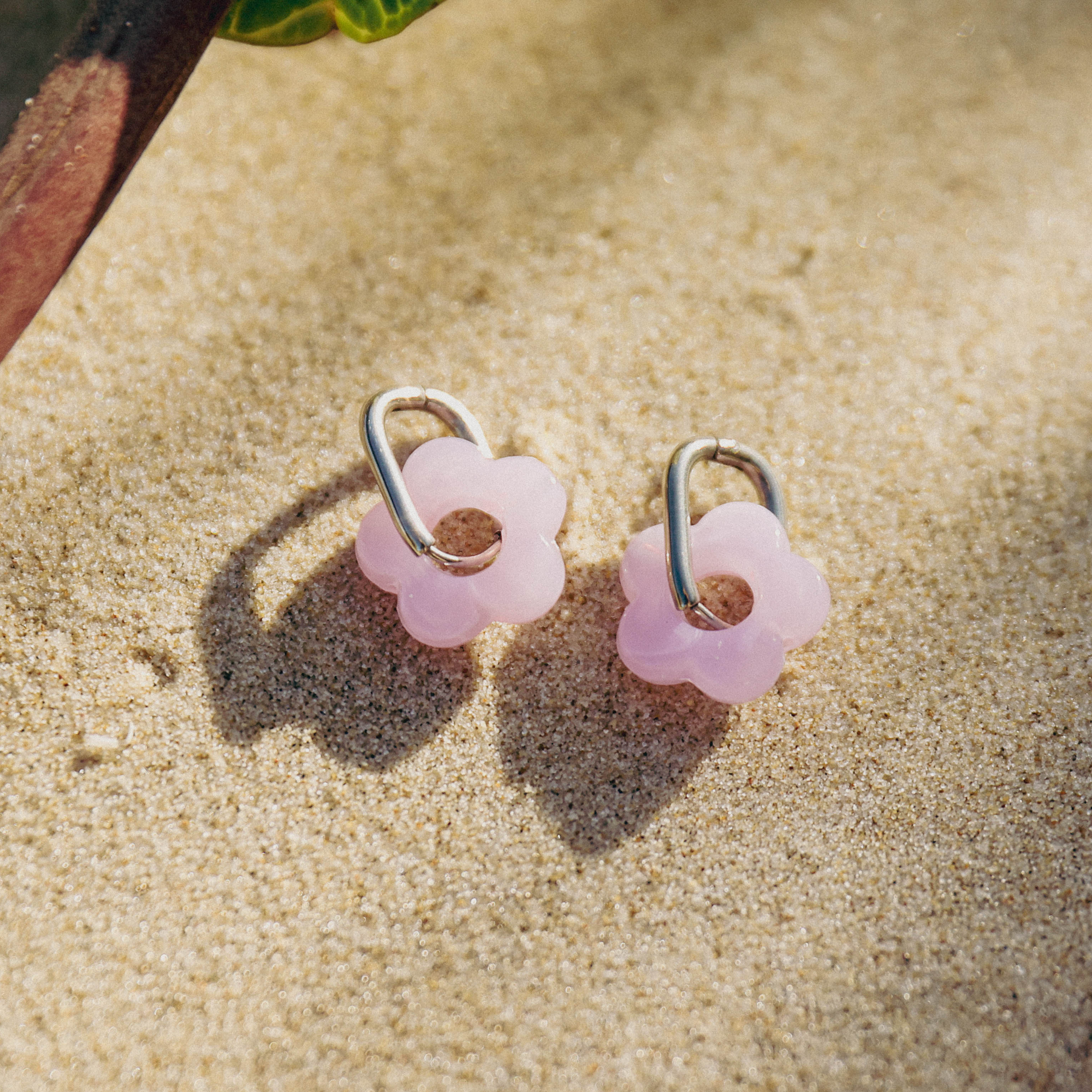 Pink flower-shaped earrings on a sandy surface