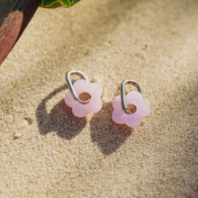 Pink flower-shaped earrings on a sandy surface