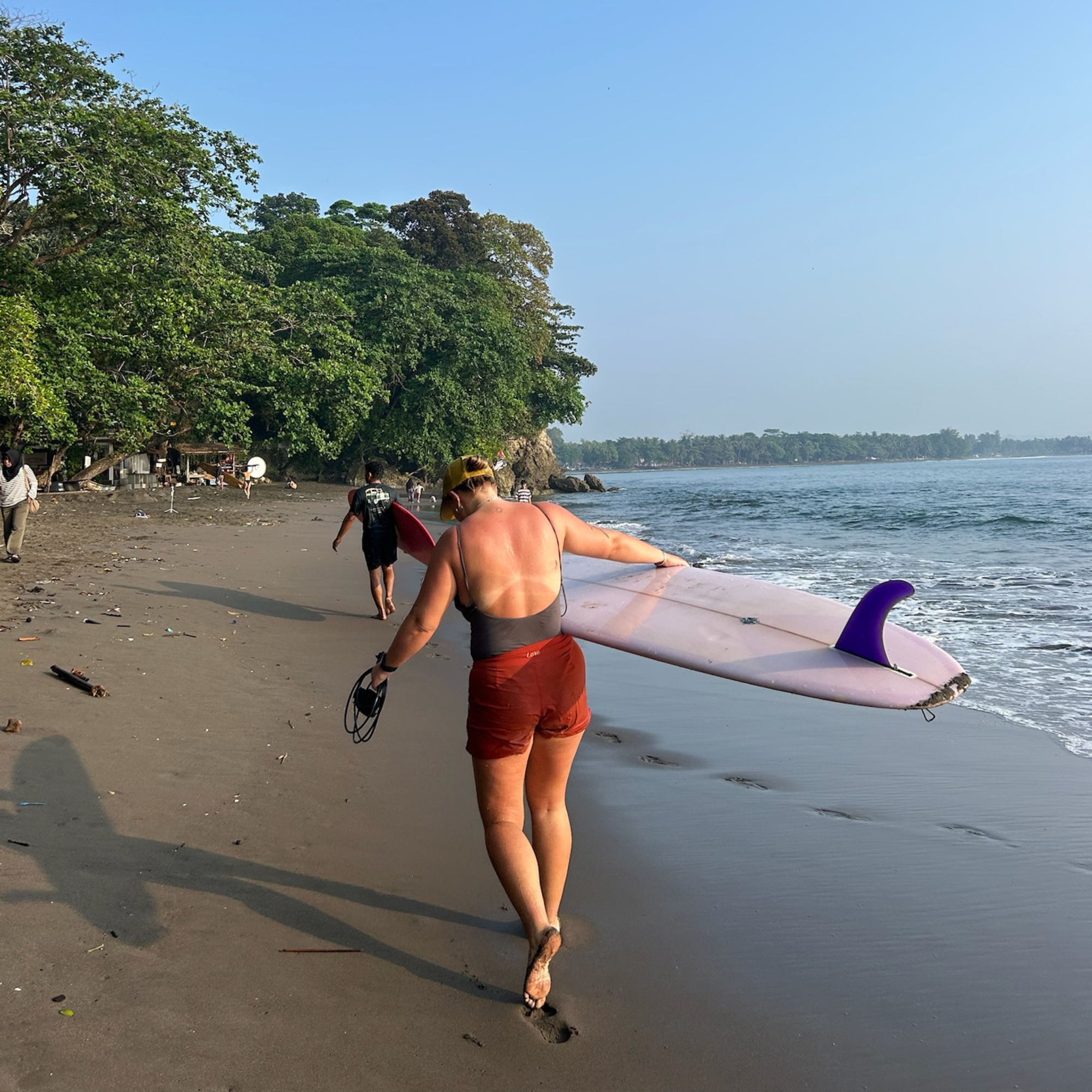 surfer walking with surfboard wearing surf boardshorts