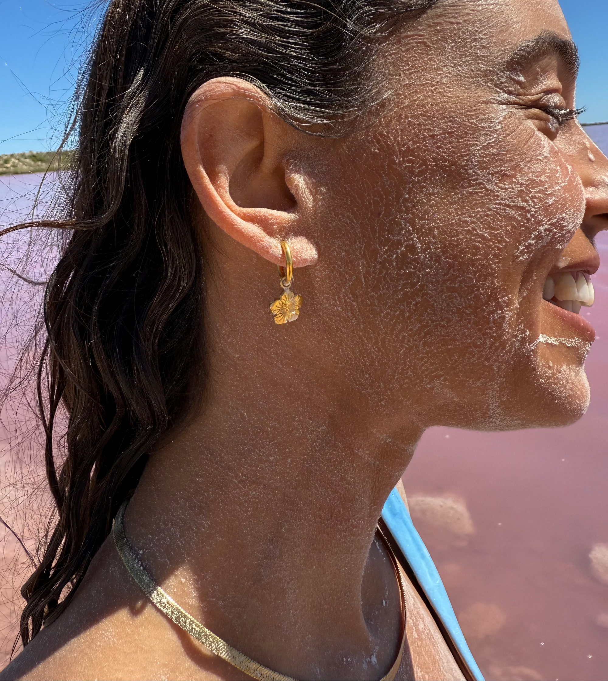 Woman with salty skin and a gold earring, standing near a pink lake